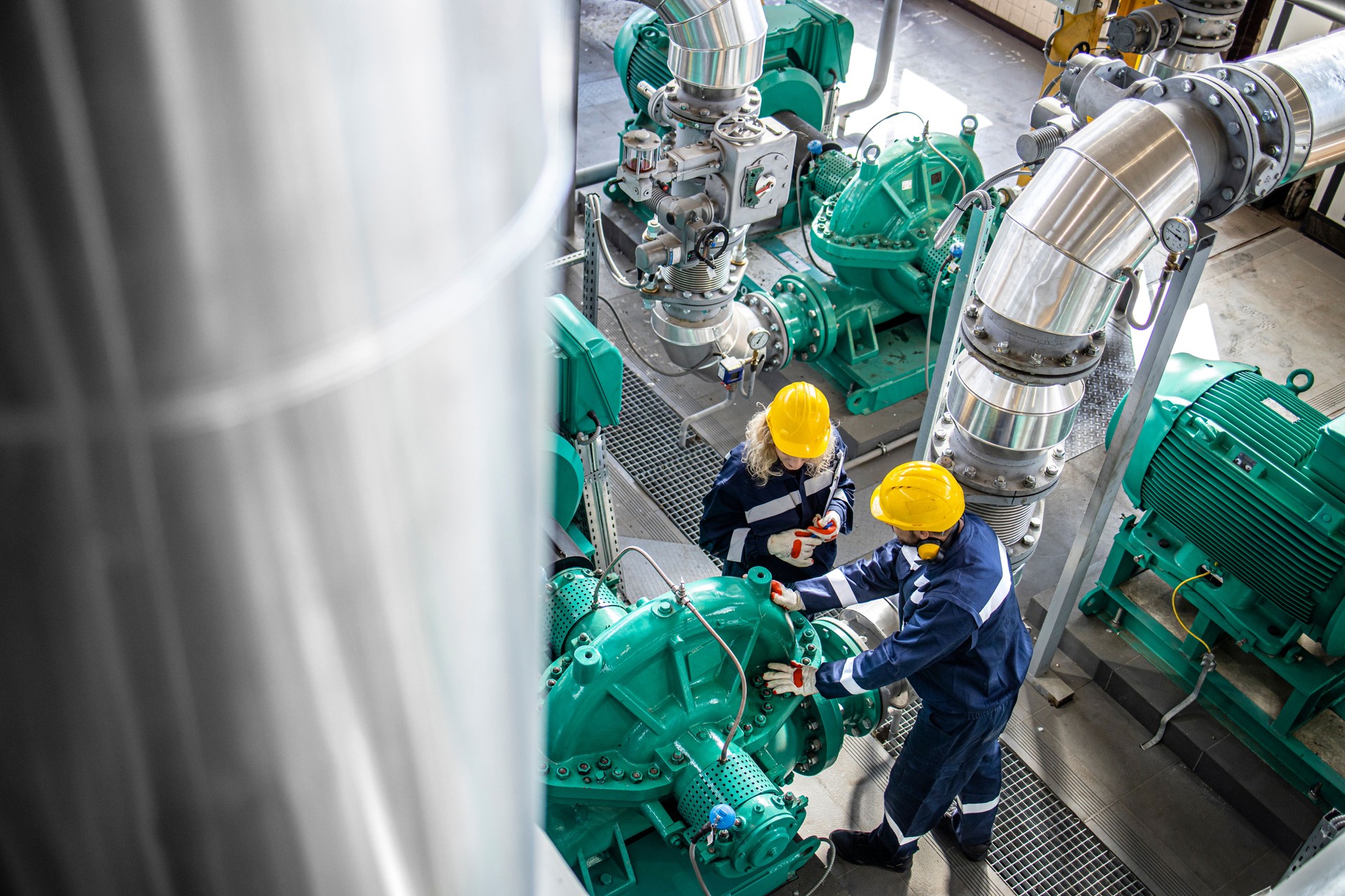 Gas and oil industrial workers working together and checking pipeline and engine pumps in factory.